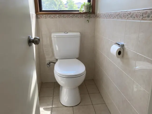 Clean white toilet in a tiled bathroom with a window and toilet roll holder in Castle Hill