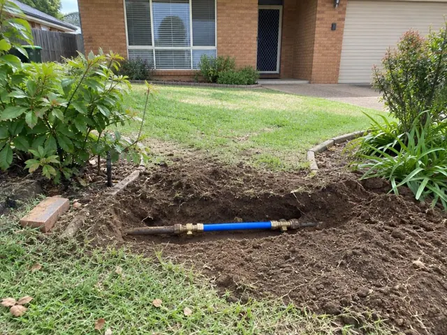 Exposed repaired water pipe in a front yard trench beside a brick house in Kellyville