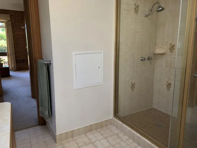 White access panel on a bathroom wall beside a tiled shower with glass screen in Glenhaven